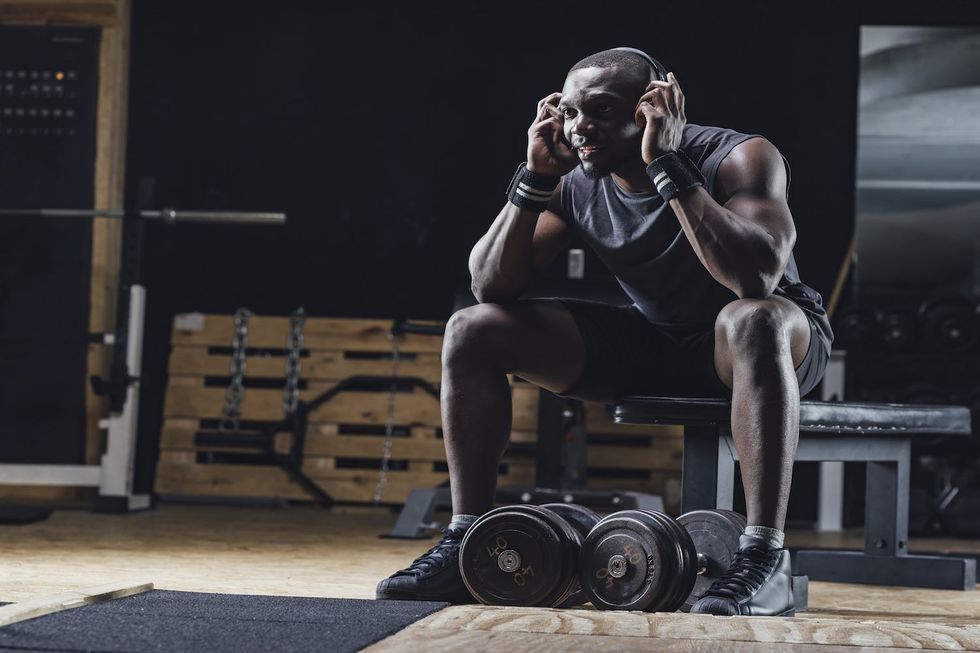 A fit Black athelete lifting weights with headphones on.