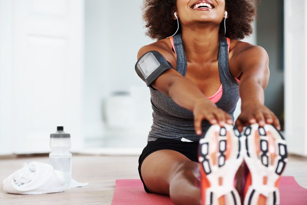 A fit smiling african american woman in gym clothing sitting on an exercise mat on her living room floor and stretching out her legs with copyspace