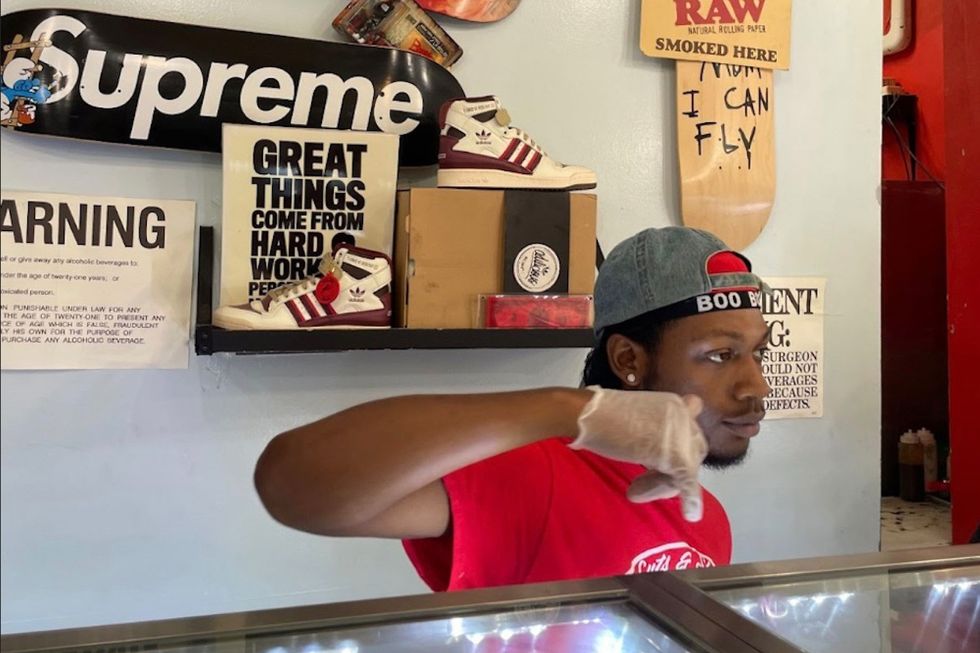 Black guy behind counter serving pizza.
