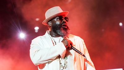 Black Thought holds a mic in an all white suite and white hat