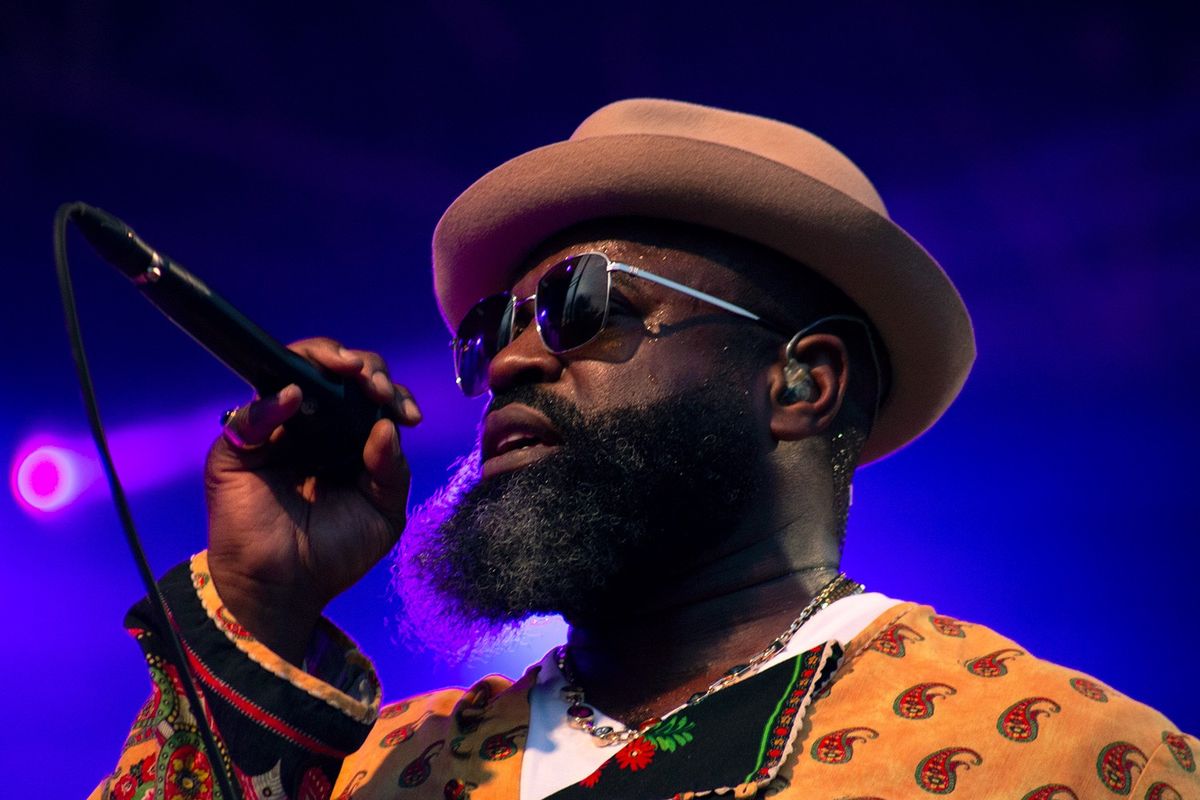 Black Thought wears a hat and sunglasses and hold a mic
