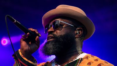 Black Thought wears a hat and sunglasses and hold a mic