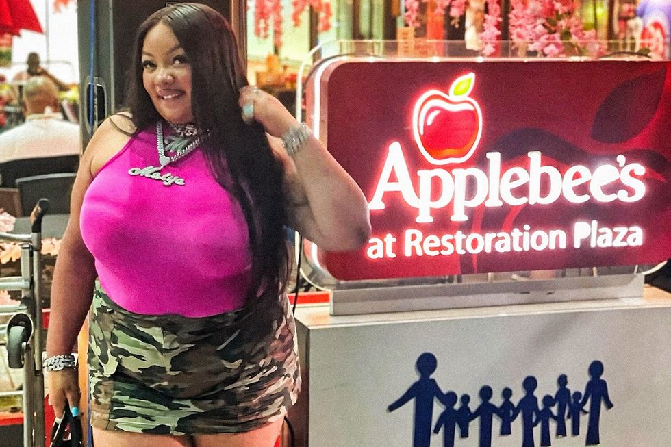 Female rapper Maiya The Don wearing a pink shirt in front of a Applebee\u2019s sign