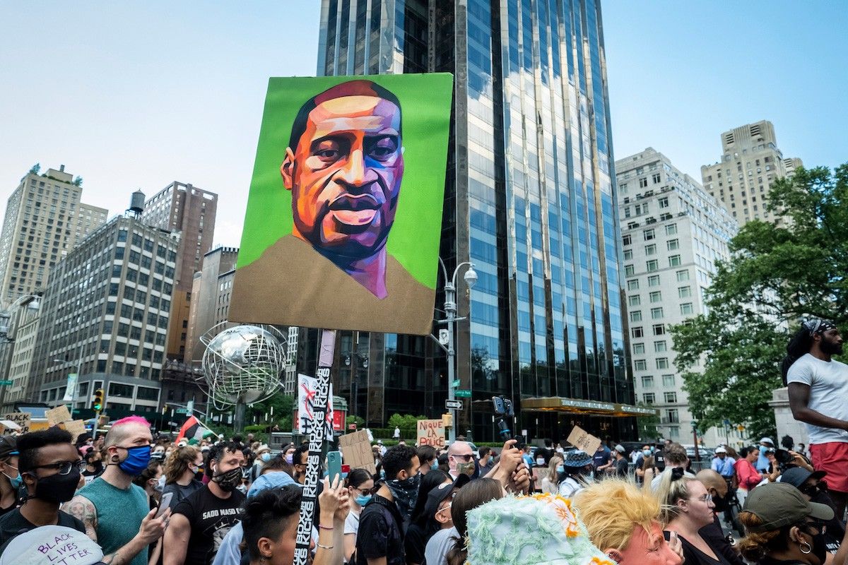 Hundreds of people pack into Columbus Circle to hear speeches against police violence while one of them holds a painted portrait of George Floyd in front of Trump International Hotel and Tower at Columbus Circle.