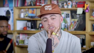 Mac Miller wearing a brown hat with gold rings 