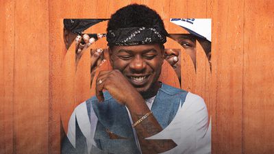Mick Jenkins smiling with chain on his arm.