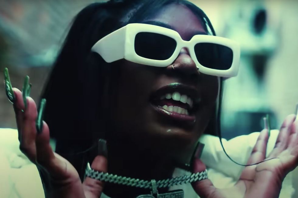 Mello Buckzz in glasses and holding her chain up for the camera. She's one of the best female rappers