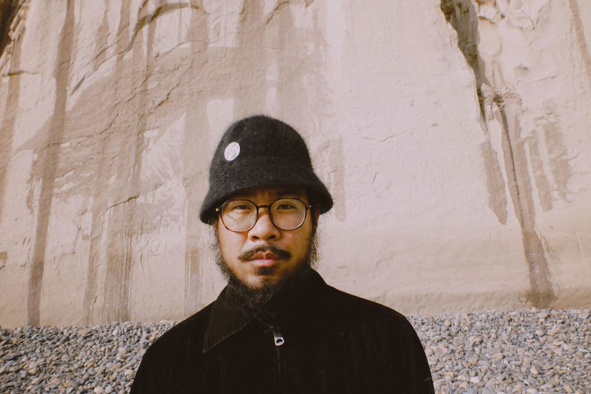 Musician and producer MNDSGN in a black bucket hat against a stone wall.