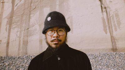 Musician and producer MNDSGN in a black bucket hat against a stone wall.