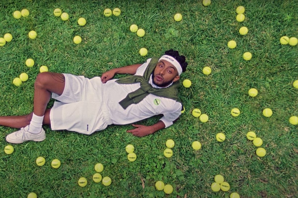Rapper Aminé laying in the grass with tennis balls