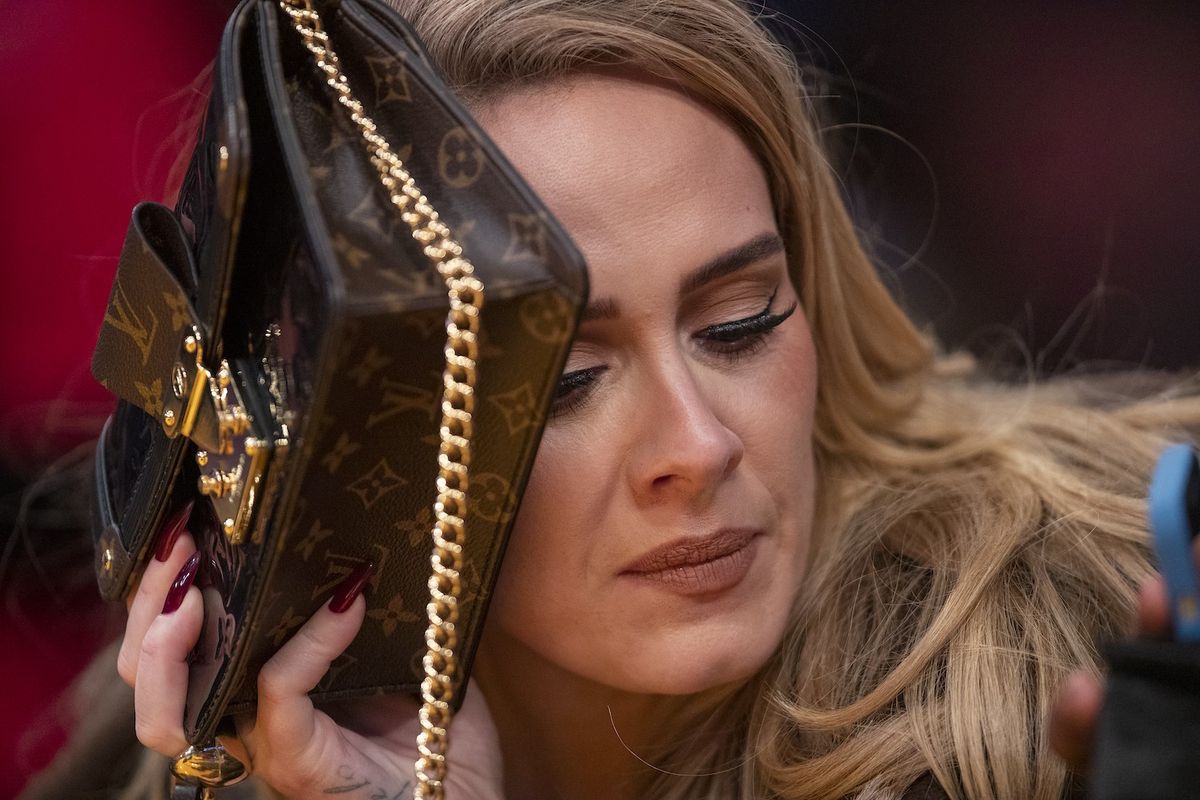 Singer Adele uses her purse to hide from the TV camera while she sings along to her song being played to the audience while attending a game between the Golden State Warriors and the Los Angeles Lakers on October 19, 2021.