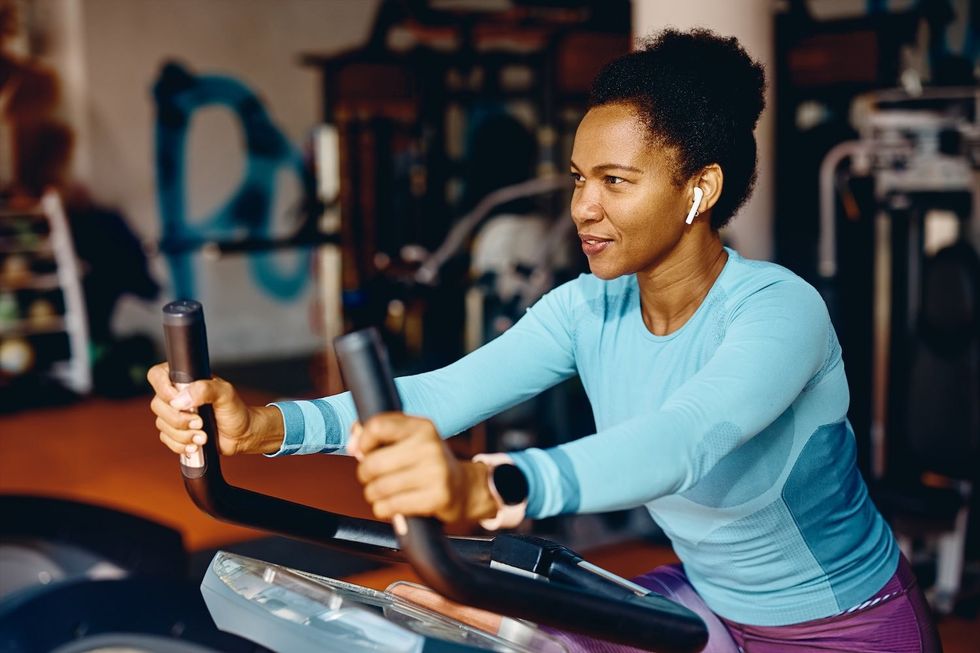Smiling African American athletic woman cycling on stationary bike in a gym.