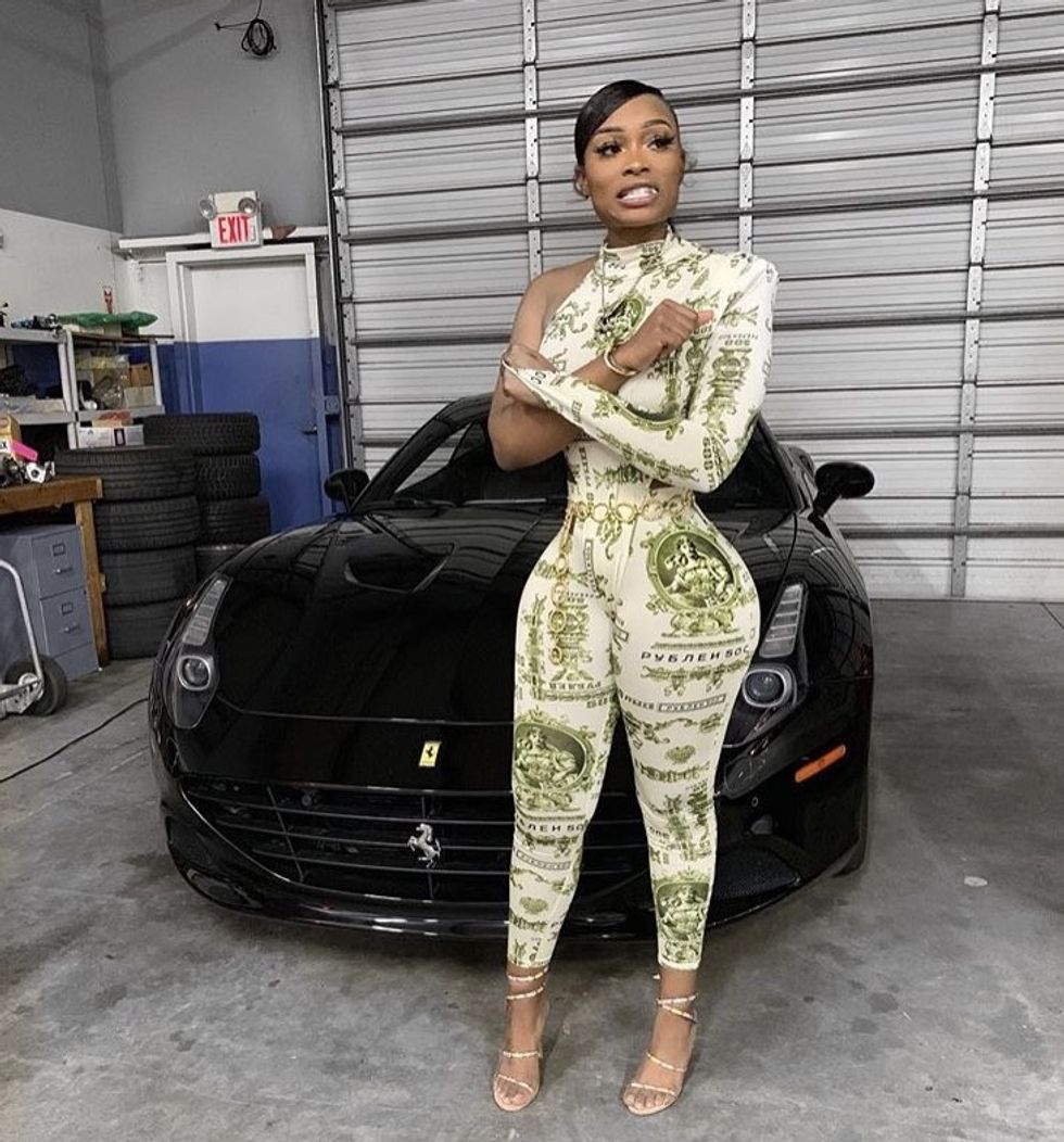 Female rapper in green print bodysuit standing in front of a Ferrari