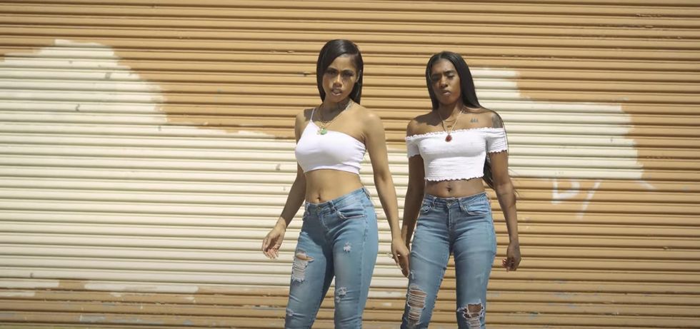 two female rappers in ripped jeans and white shirts in front of garage door