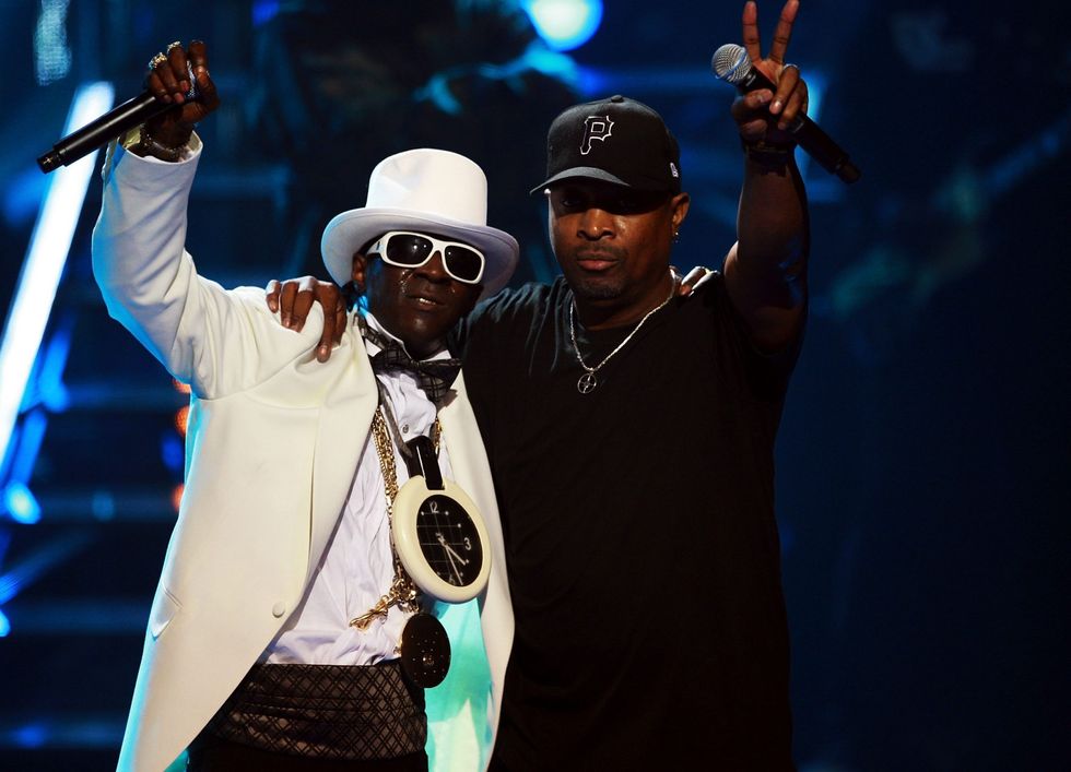 Flavor Flav, wearing all white and hat, Chuck D, wearing black shirt and hat.