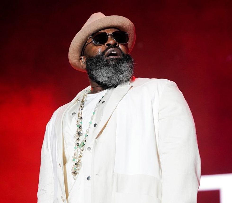 Black Thought wears an all-white suit and stands in front of a red background