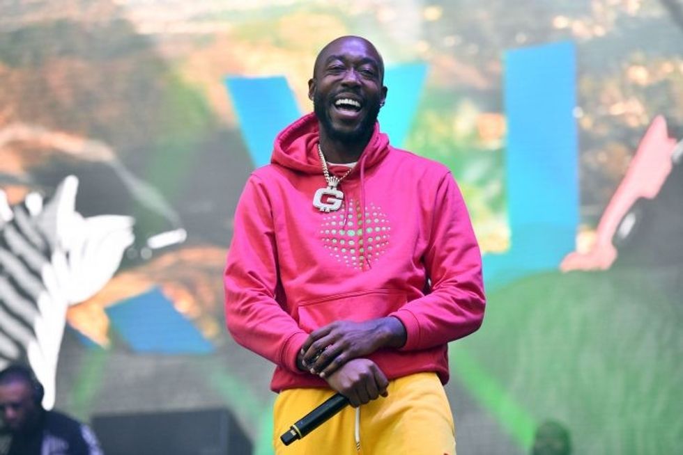 Freddie Gibbs smiling on stage with a pink hoodie on