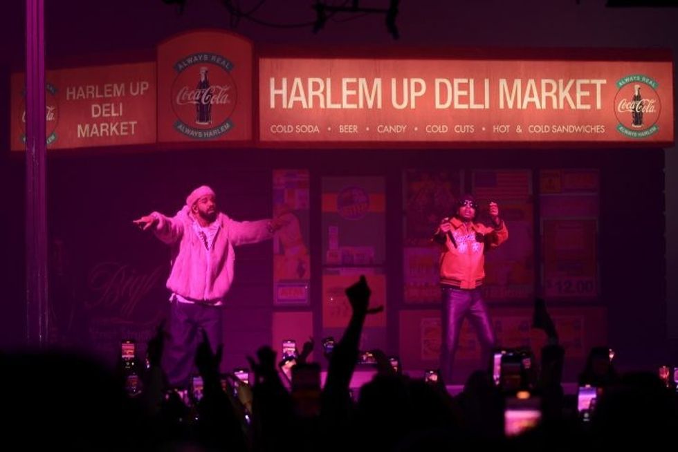 Drake on stage in a pink mink coat with 21 Savage next to him on stage in front of a bodega set.