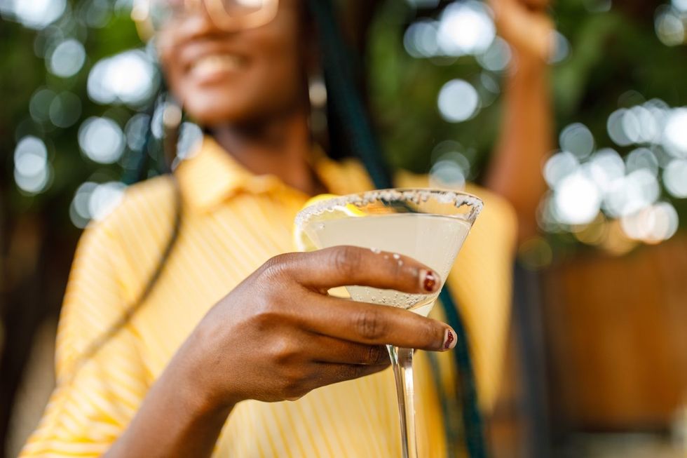Low angle view of cheerful young woman holding and enjoying a martini glass with margarita cocktail at a cocktail bar