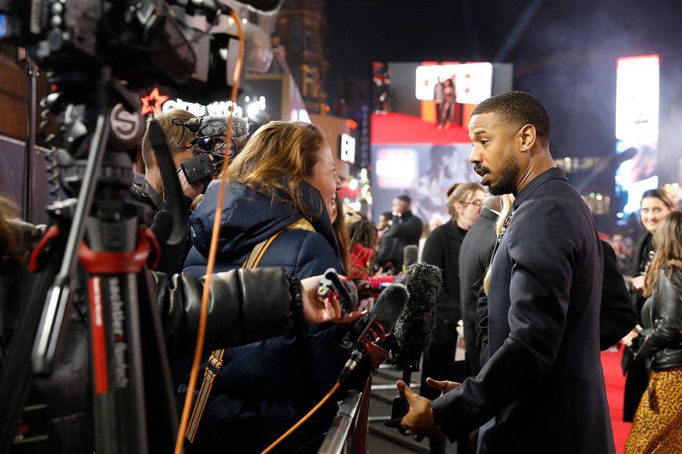 Michael B. Jordan at the premiere of Creed III dressed in a suit and speaking to reporters. 